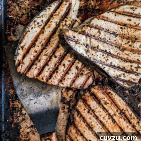 Several grilled fish fillets on a baking sheet with a spatula underneath them.