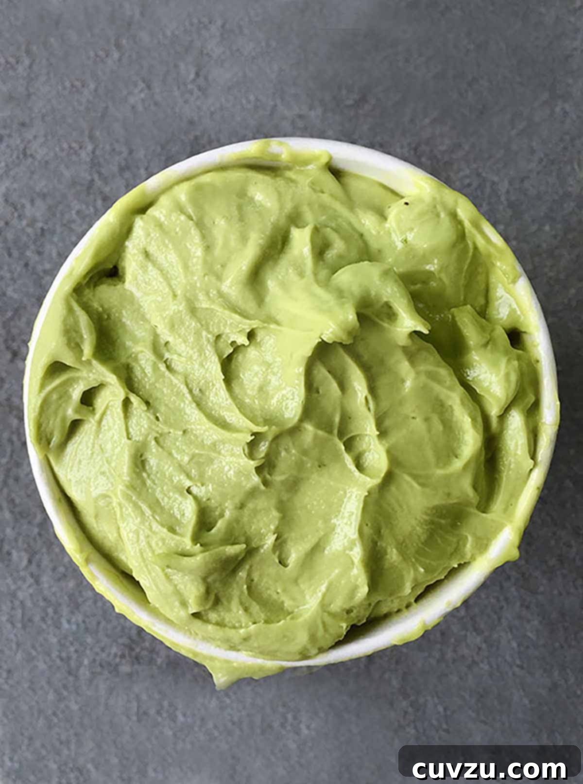 A container of green avocado sorbet on a slate surface, garnished with a lime wedge.