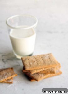 A pile of homemade graham crackers on a marble table with a glass of milk nearby.