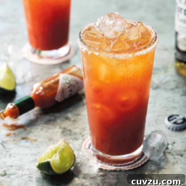 A glass filled with Mexican Bloody Mary, garnished with a lime wedge, sitting next to slices of lime.