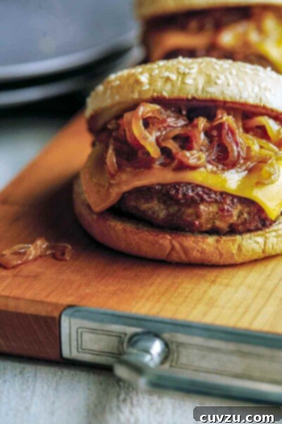 A turkey burger with maple caramelized onions and cheese on a wooden cutting board.