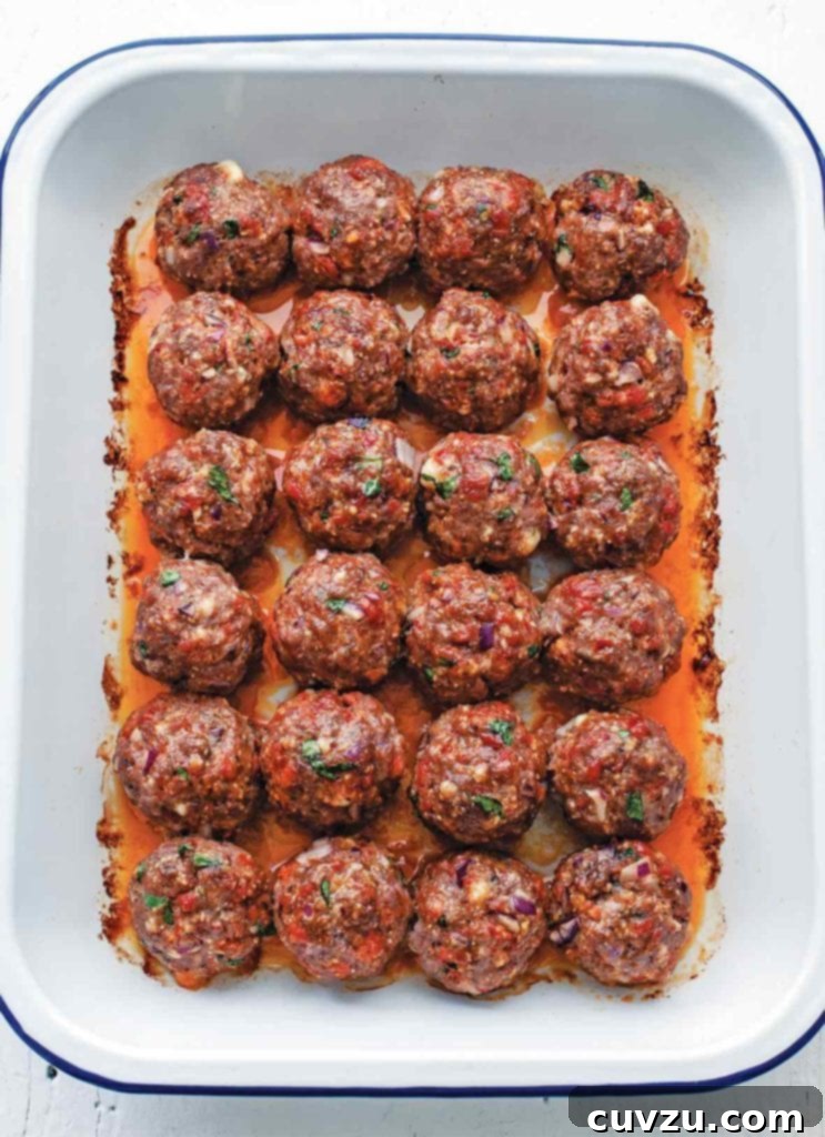 Tapas-Style Chorizo Meatballs 2 A white pan filled with approximately 24 perfectly round, orange-red chorizo meatballs, each about golf-ball size.