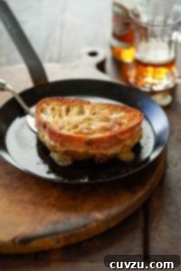 A black metal skillet with a spatula ready to flip a Welsh rarebit grilled cheese sandwich.
