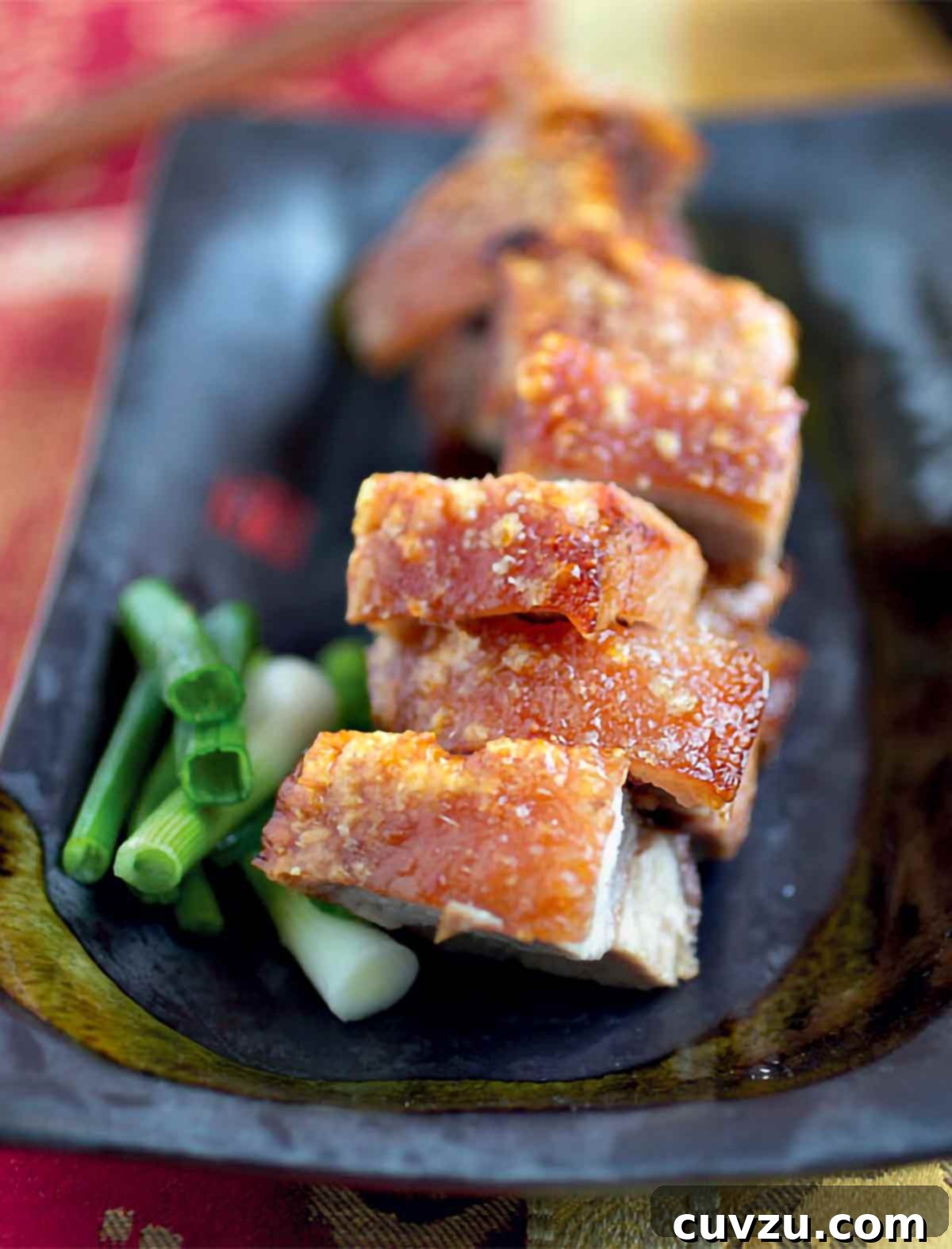 Golden Crispy Chinese Roast Pork 2 Pieces of Chinese roast pork in a black dish with chopped scallions beside it.