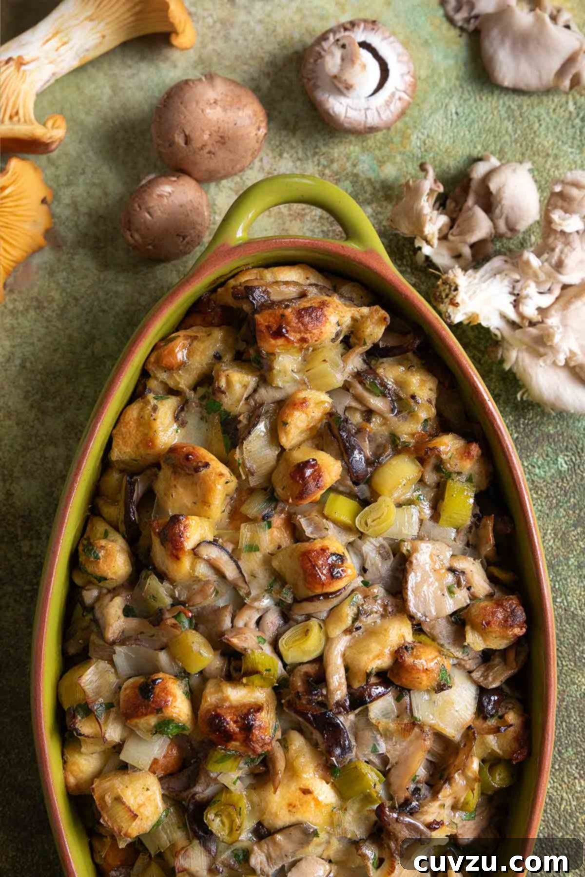 An oval casserole dish filled with golden-brown wild mushroom stuffing, garnished with fresh herbs.