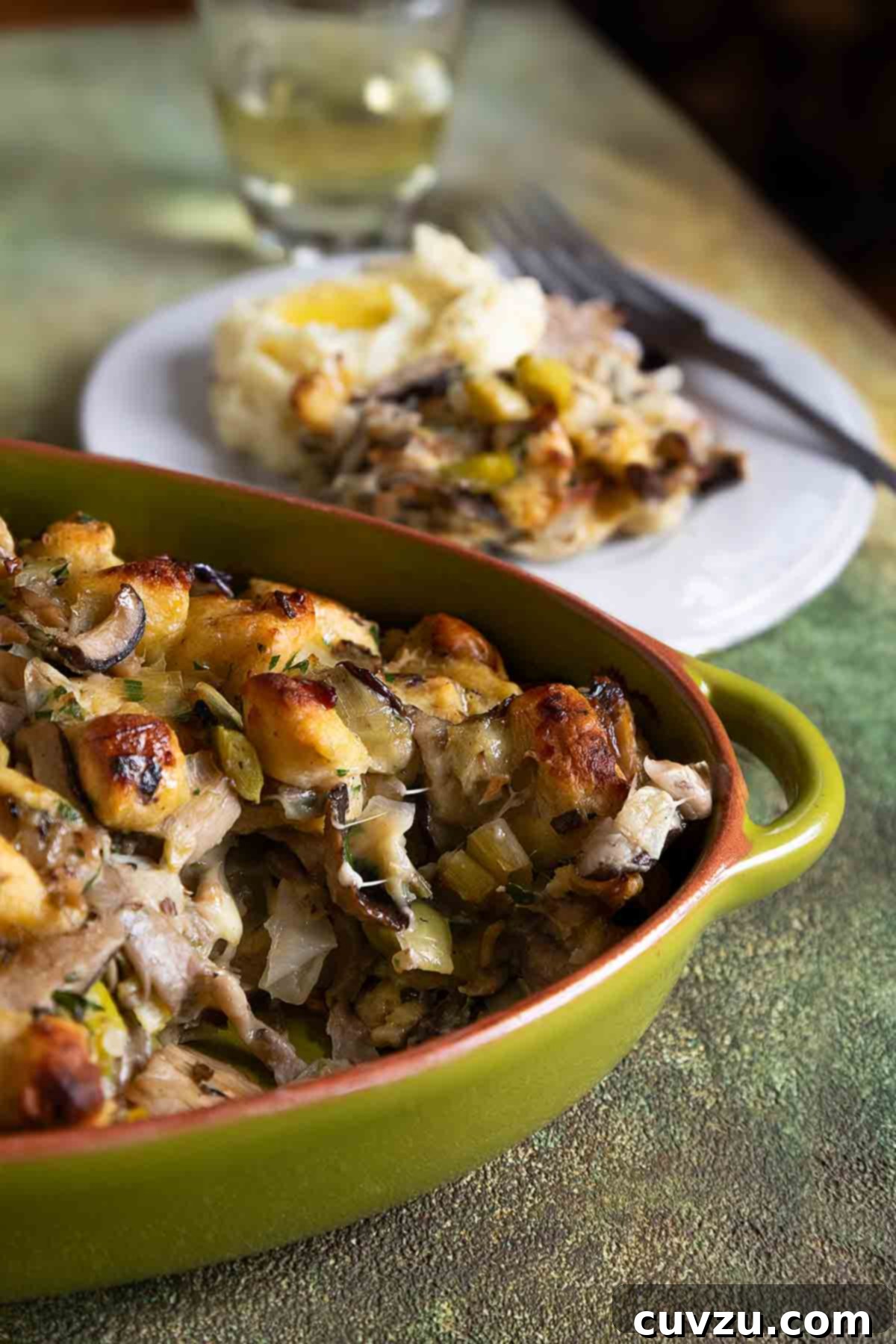 An oval casserole dish filled with wild mushroom stuffing, and a plate of stuffing and mashed potatoes next to it.