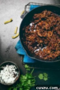 A cast iron pot filled with braised short rib chili with a bowl of diced onion on the side and a handful of cilantro.