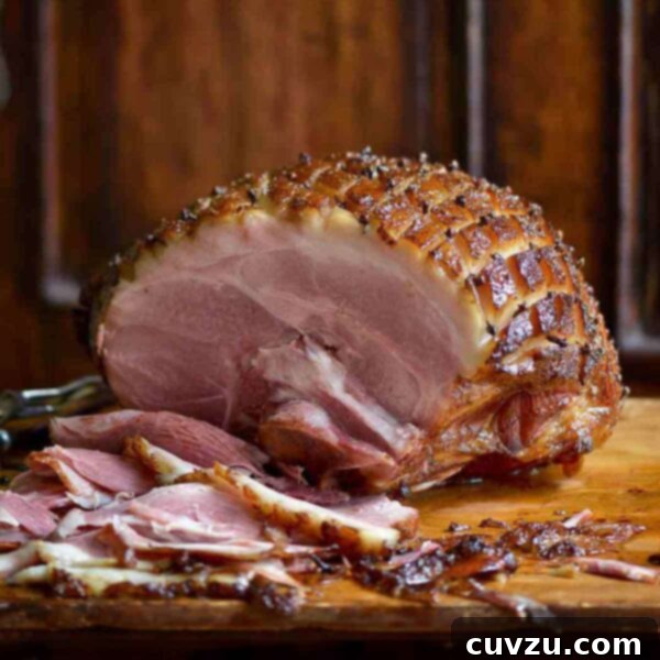 A partially carved mustard-glazed ham, cross-hatched and studded with cloves on a wooden cutting board.