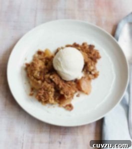 A piece of apple crumble topped with vanilla ice cream in a white bowl.