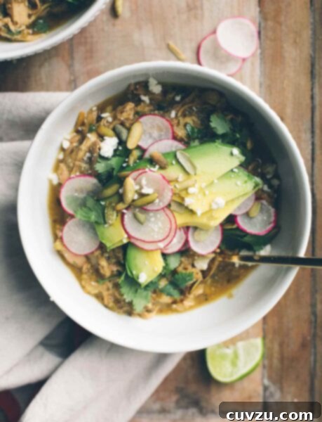 A white bowl filled with pozole verde, topped with sliced radishes, pepitas, avocado, and cilantro.