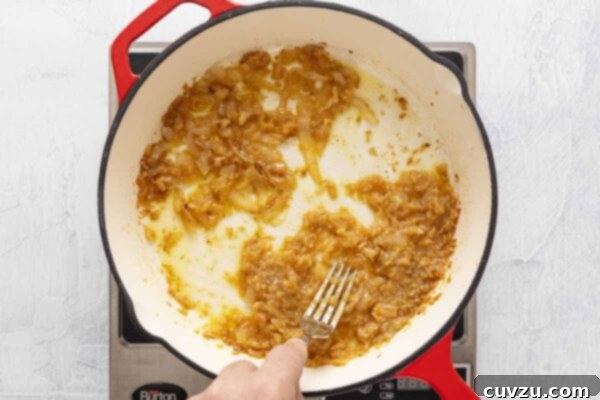 Egg Salad Reinvented 12 A person mashing caramelized onion and garlic together in a skillet.