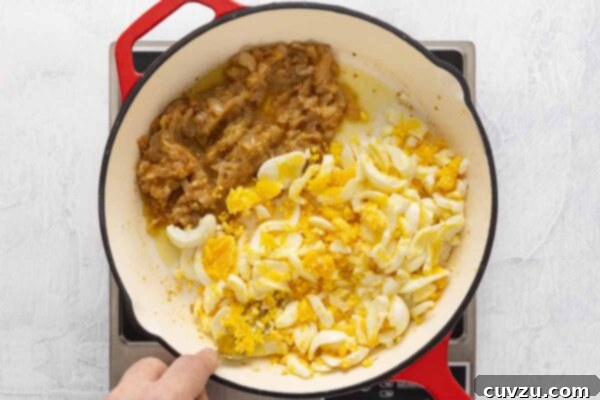Egg Salad Reinvented 13 A person mashing hard-boiled eggs into a skillet with caramelized onions and garlic.