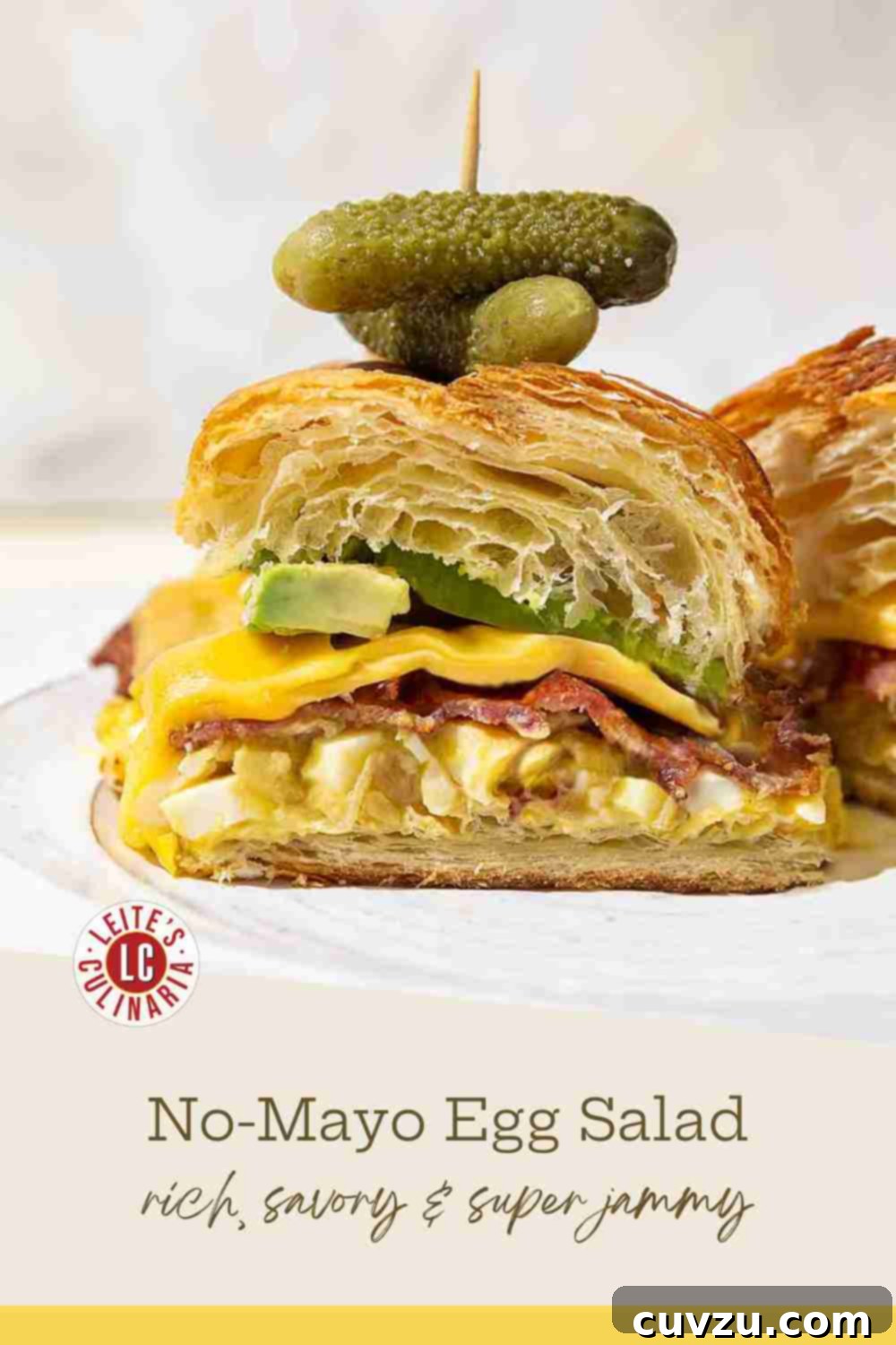 Egg Salad Reinvented 3 A croissant sandwich filled with mayo-free egg salad, crispy bacon, cheese, and avocado slices, with a pickle on top.