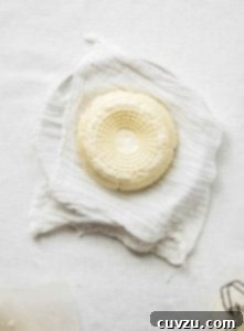 Homemade Farmer Cheese 3 A round of farmers cheese resting on a piece of cheesecloth in a bowl.