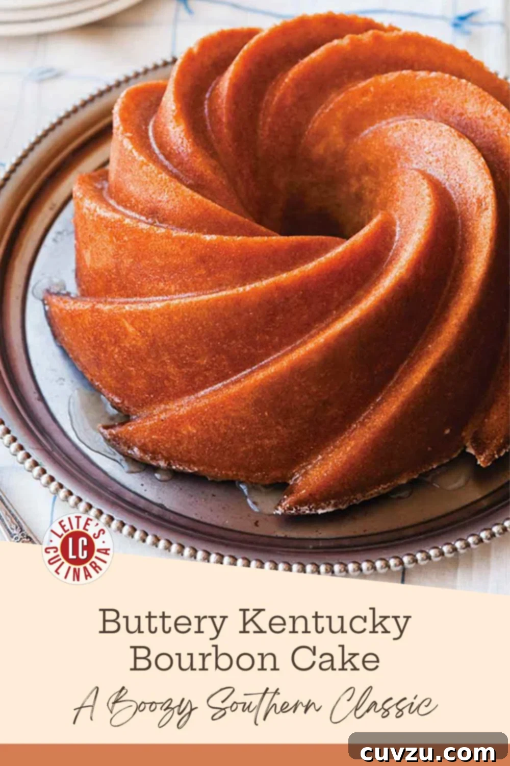 A golden-brown bourbon Bundt cake, elegantly drizzled with a glistening glaze and resting on a polished silver platter, evoking Southern charm.