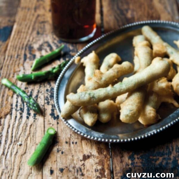 A silver platter filled with asparagus tempura with some pieces of asparagus and a glass of beer on a wooden table.