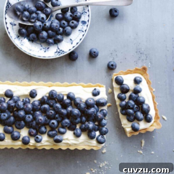 A close-up view of the rectangular blueberry mascarpone tart, with a single slice removed to showcase the smooth, lemon-infused filling and a generous topping of fresh, glistening blueberries.
