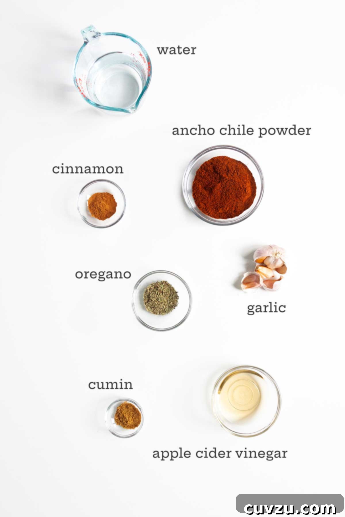 A collection of ingredients laid out for homemade adobo sauce, including vibrant chile powder, fresh garlic, and an assortment of aromatic spices and vinegar.
