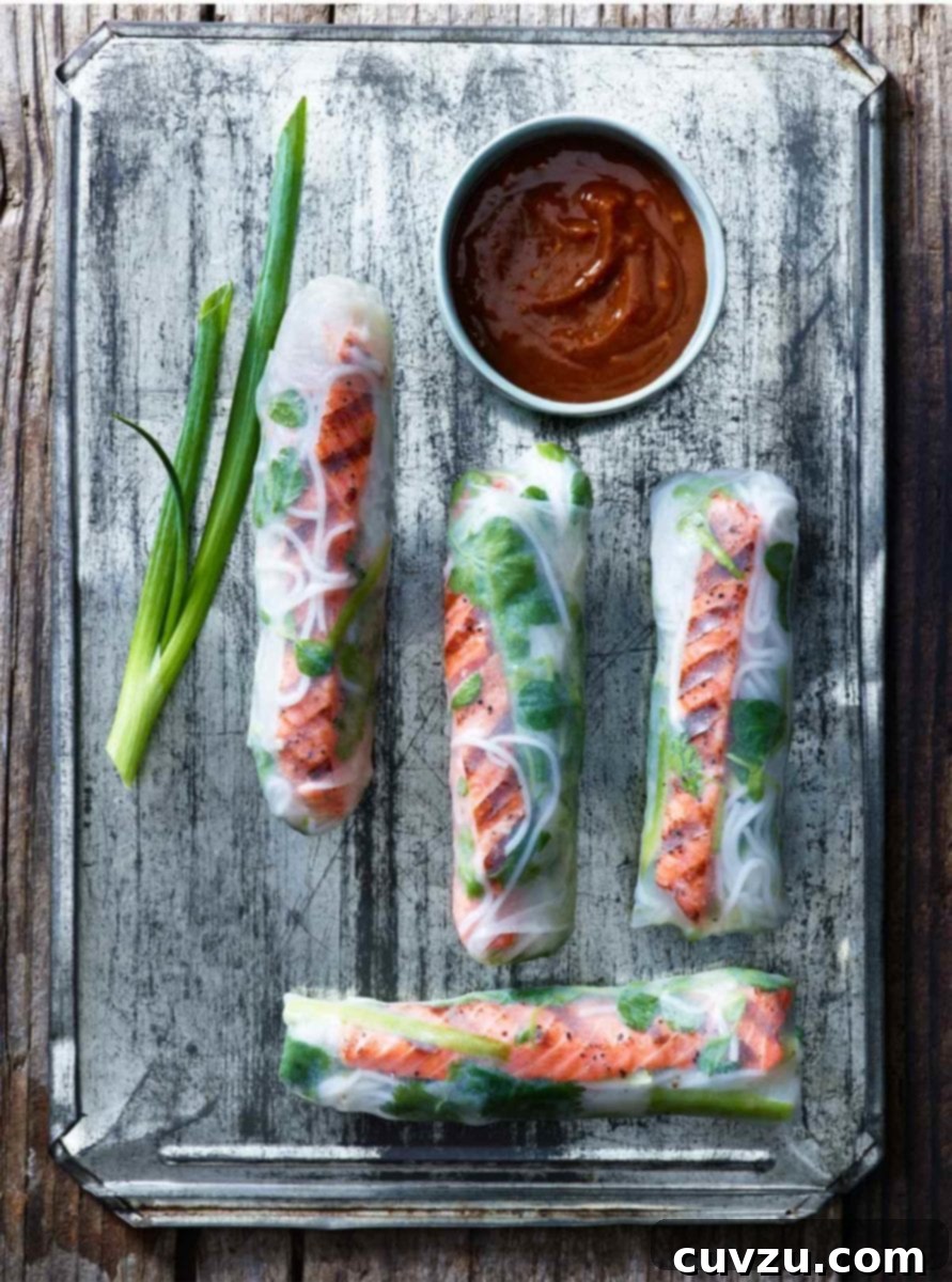 Refreshing Salmon Summer Rolls 2 Four salmon summer rolls on a metal sheet with a piece of scallion and a bowl of dipping sauce.
