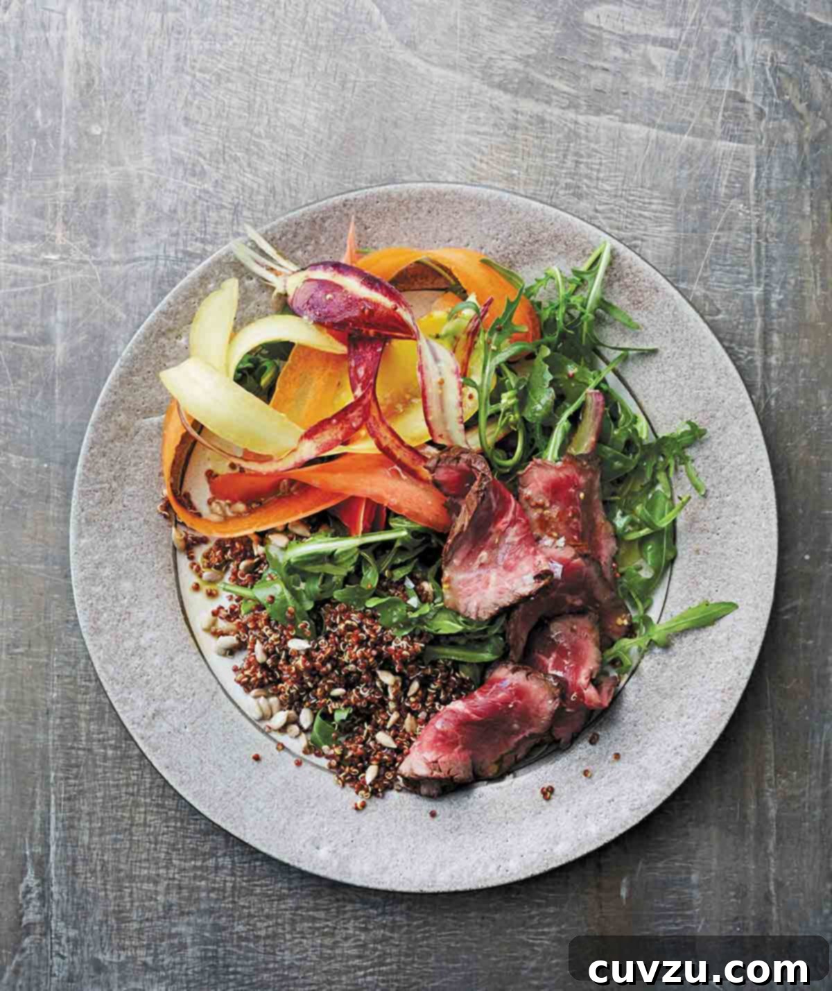 Grilled Steak and Quinoa Power Salad 2 A vibrant grey plate topped with slices of perfectly cooked steak and fluffy quinoa salad, garnished with delicate shaved carrots and drizzled with a tangy whole-grain mustard vinaigrette.