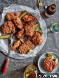 A platter of pickle-brined fried chicken with pieces of dill pickle, and a bottle of beer.