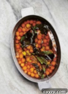 A Dutch oven filled with a cherry tomato confit of Sun Gold cherry tomatoes, oil, and fresh basil leaves.