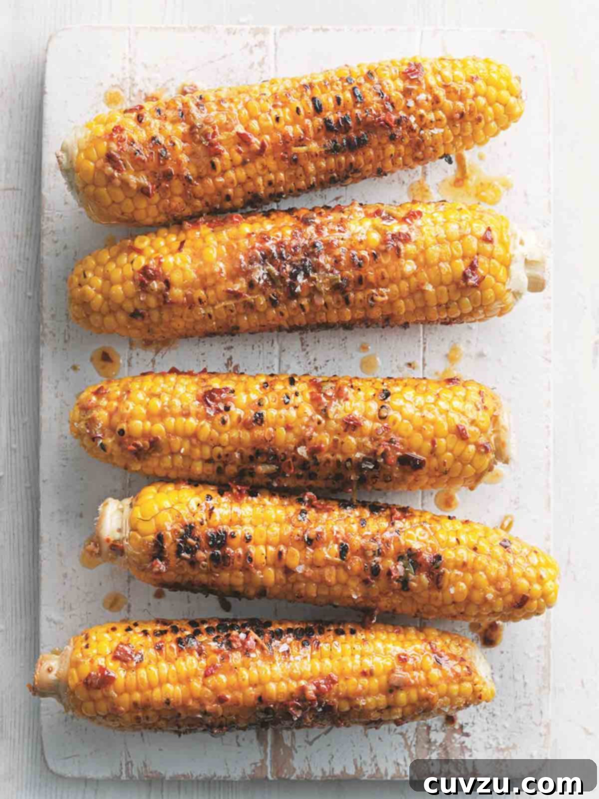 Five ears of grilled corn on the cob with chipotle butter on a white wooden board, ready to be served.