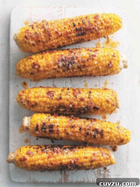 Five ears of grilled corn on the cob with chipotle butter on a white wooden board.