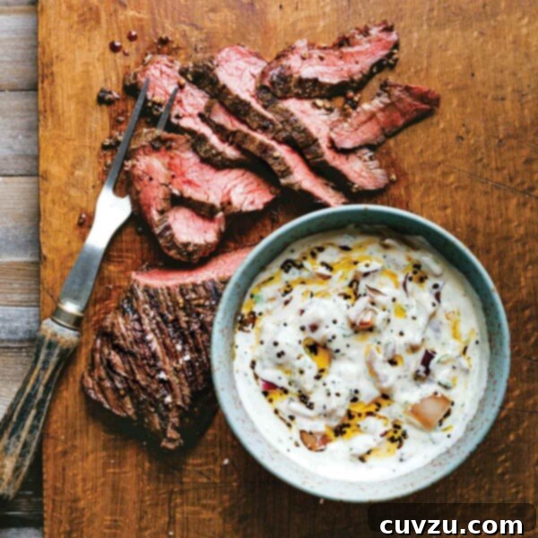 A sliced grilled hanger steak with raita in a bowl next to it on a wooden cutting board.