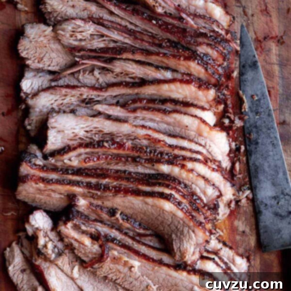 A sliced Texas brisket on a wooden board with a knife lying beside it.
