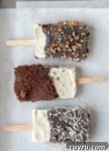 Three homemade ice cream bars, coated with chocolate and sprinkled with almonds, coconut, and chocolate crumbs.