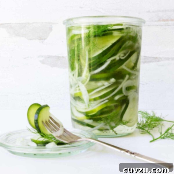 Two jars of refrigerator sweet pickles, one with a dill sprig, sitting on a wooden surface.