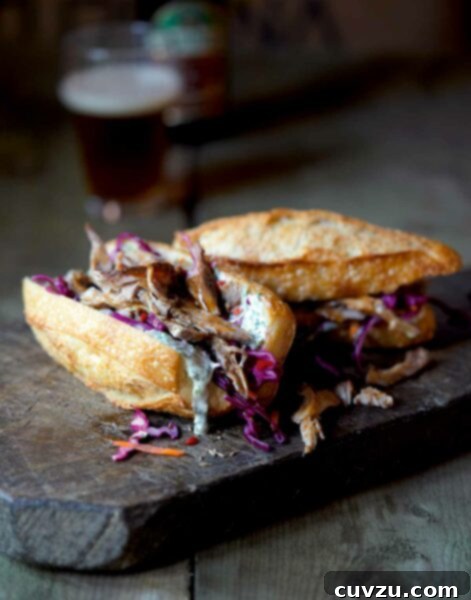 A wooden cutting board with two pulled pork sandwiches in crusty buns and topped with coleslaw, with a bottle and glass of beer in the background, inviting a delicious meal.
