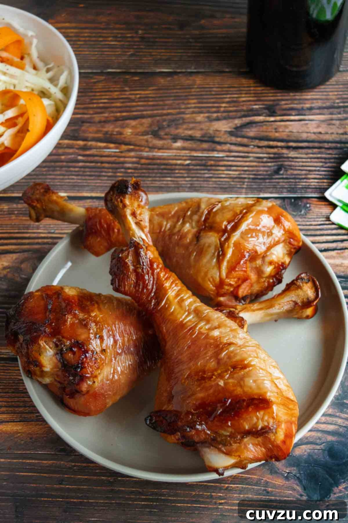 Savory Smoked Turkey Legs 7 Three perfectly smoked turkey legs arranged on a plate with a bowl of fresh, vibrant coleslaw in the background, ready to be served.