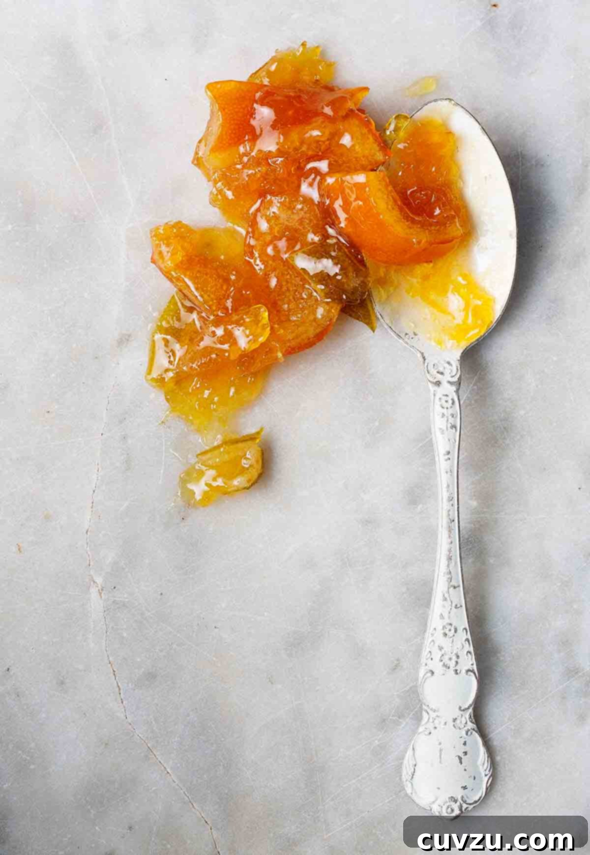 Sunshine Citrus Marmalade 2 A spoonful of homemade mixed citrus marmalade spilling over onto a grey marble surface, showcasing its vibrant color and chunky texture.
