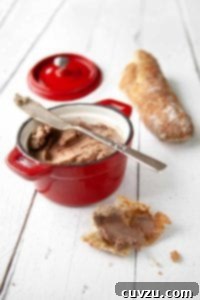 A small red crock of easy chicken liver pate, nearby a baguette and a hunk of bread smeared with pate