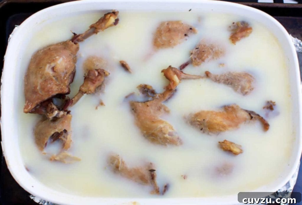 A white oval casserole dish filled with gloriously golden-brown duck confit legs, ready to be served.