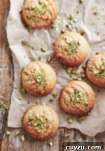 Six tahini cookies on a piece of parchment with chopped pistachios on the cookies and on the parchment.