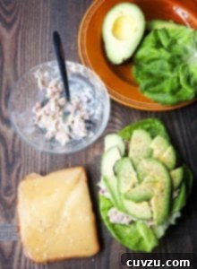 The makings of a Mediterranean tuna melt -- a slice of whole grain bread topped with gruyere cheese, a bowl with tuna salad, and a butter lettuce leaf topped with tuna salad, avocado, and pepper