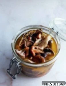 A canning jar filled with pickled wild mushrooms and a sprig of thyme.