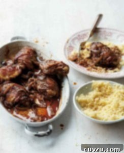 An oval dish filled with Baharat spiced chicken pieces and a bowl of couscous and plate of couscous and chicken on the side. Close-up of roasted chicken.