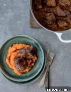 Decadent Maple Bourbon Braised Short Ribs 3 A green plate containing sweet potato puree, topped with 2 pieces of short rib. A Dutch oven is beside the bowl with more short ribs.