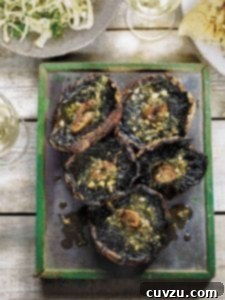 A metal platter holding five grilled portobello mushrooms, topped with glistening garlic rosemary butter, ready to be served.