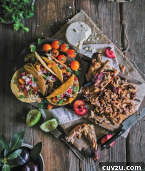 A black platter presenting an appetizing arrangement of grilled chicken tacos, garnished with colorful fruit salsa and cherry tomatoes. Also visible is a wooden cutting board with sliced grilled chicken, halved plums, and crumbled queso fresco.