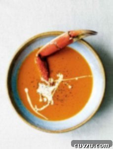 A bowl of creamy crab soup drizzled with cream, and sprinkled with pepper, with a crab leg sticking out of it.
