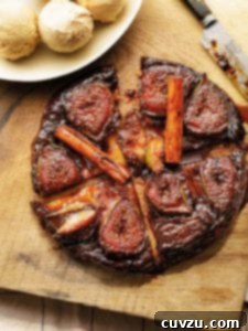 A fig tarte tatin, sliced into four pieces with cinnamon sticks on top. Nearby a bowl of ice cream.