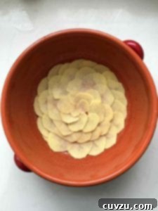 Portugal's Iconic Salt Cod Bake 4 Close-up of layers of potatoes, onions, and salt cod within a red clay pot, showcasing the meticulous assembly of Bacalhau à Gomes de Sá.