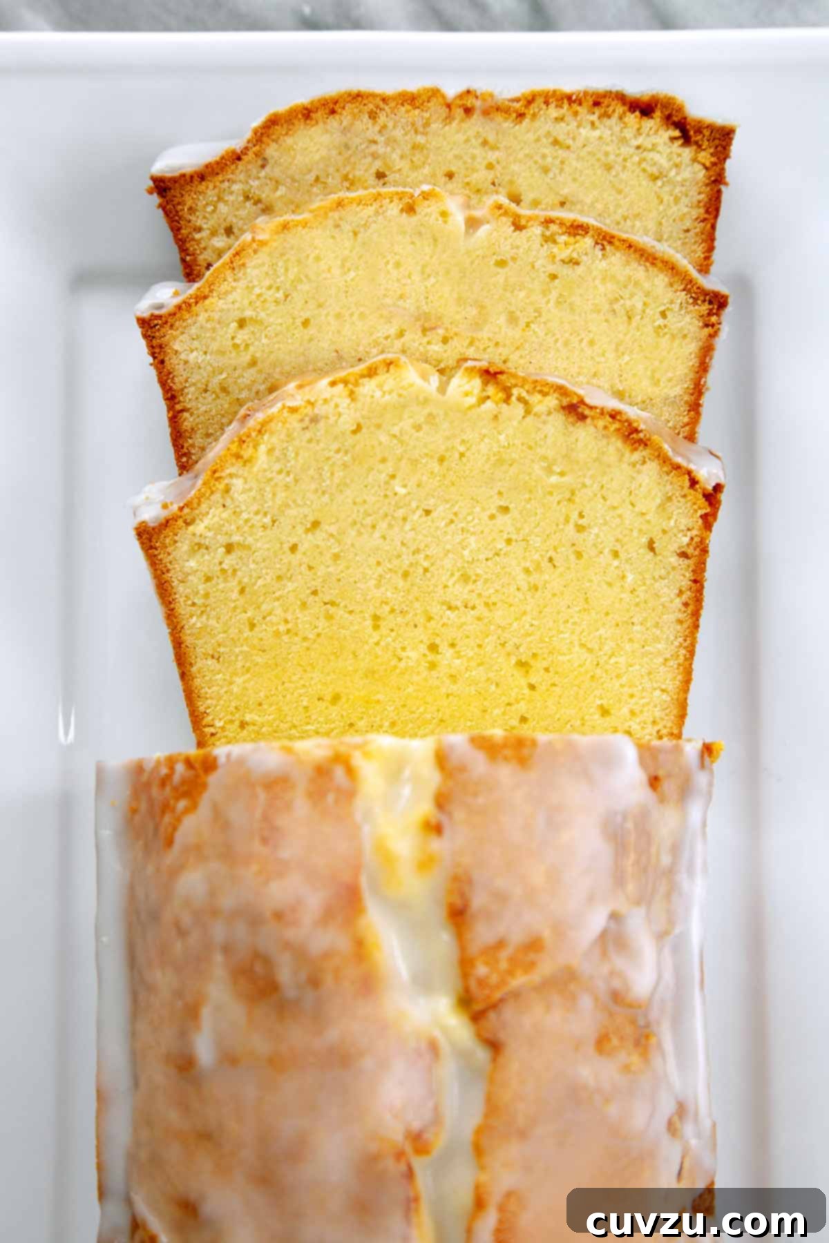 Velvet Cream Cheese Pound Cake 2 A partially sliced loaf of cream cheese pound cake with lemon glaze, showcasing its moist texture.