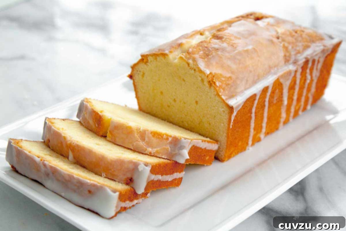 Velvet Cream Cheese Pound Cake 3 A partially sliced loaf of cream cheese pound cake, glazed and ready to serve.