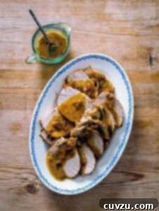 Braised pork loin with rosemary topped with a mustard-garlic sauce on a white plate on wood